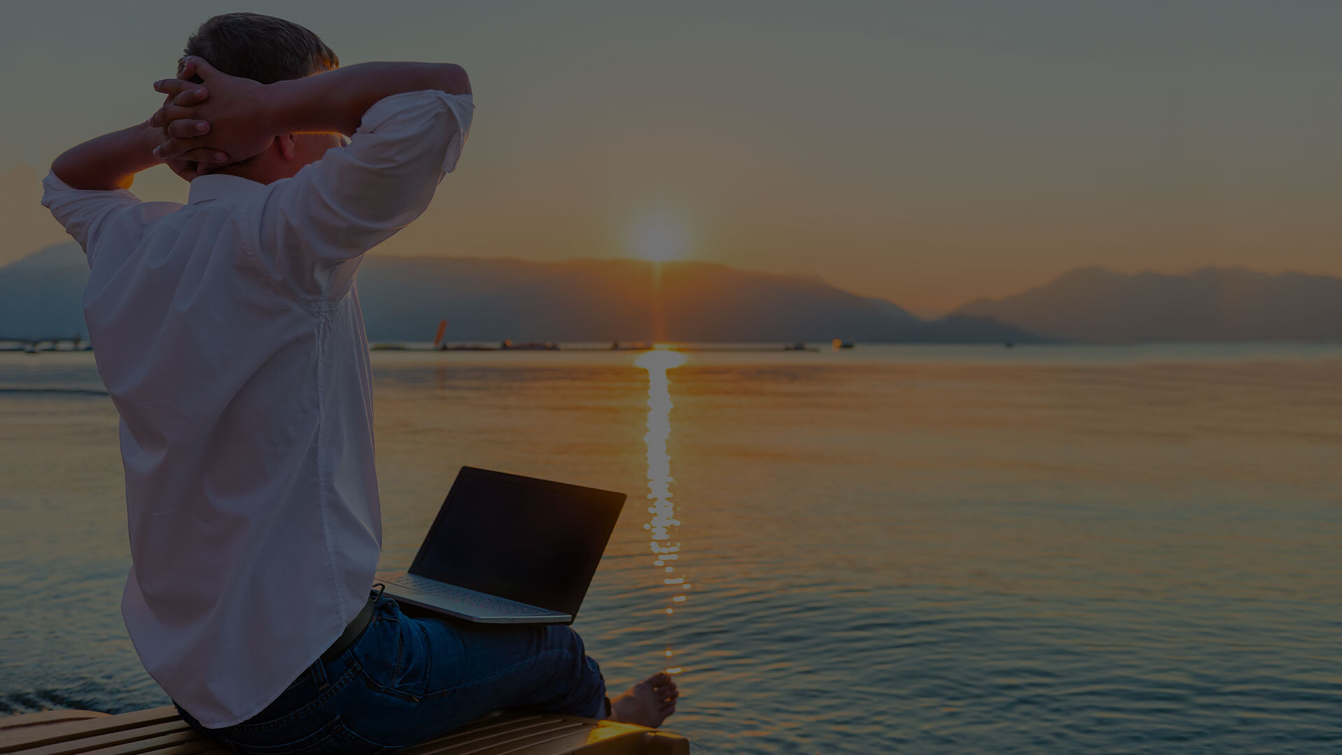 work-life freedom | person sits on beach with their arms behind their head, relaxing with their laptop in their lap