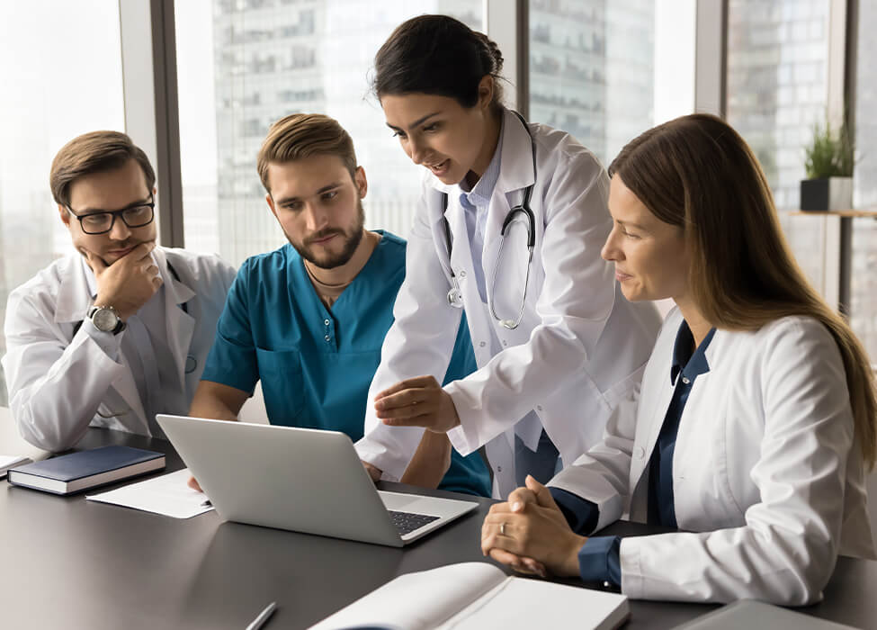 A group of healthcare professionals in a meeting, gathered around a laptop as they discuss patient care strategies or review a medical coding audit. The diverse team includes doctors and specialists focused on collaborative decision-making.