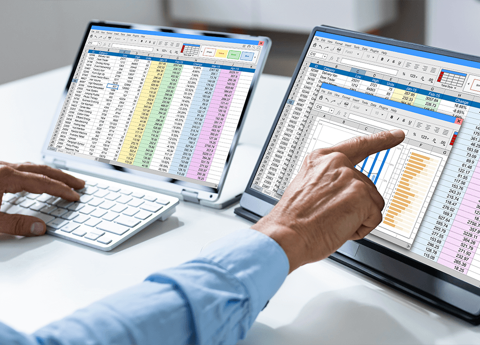 Two professionals analyzing financial data on dual laptop screens showing detailed spreadsheets and charts in an office environment.