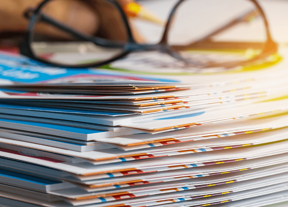Close-up of a stack of colorful, printed brochures and magazines, with a pair of glasses on top, highlighting the output of managed print services.