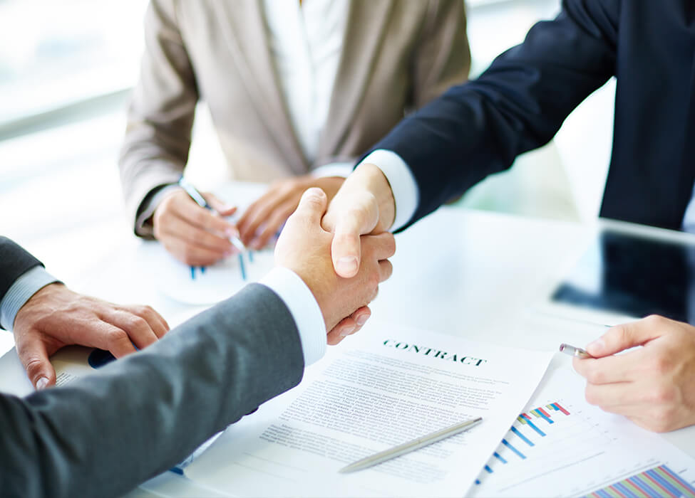 Two people shaking hands over a contract that rests on the table in between them